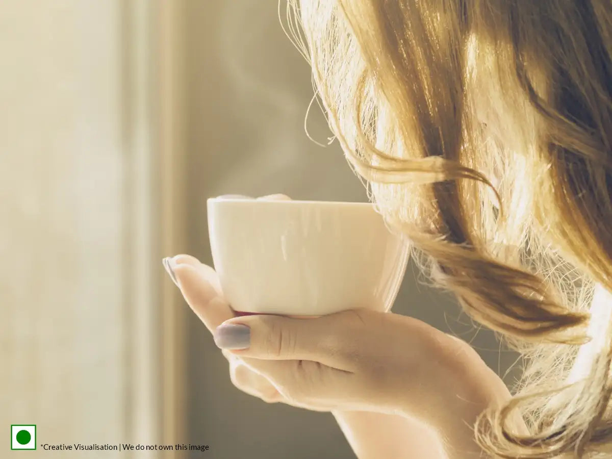An image of a woman holding a cup of tea in the early hours of the morning.