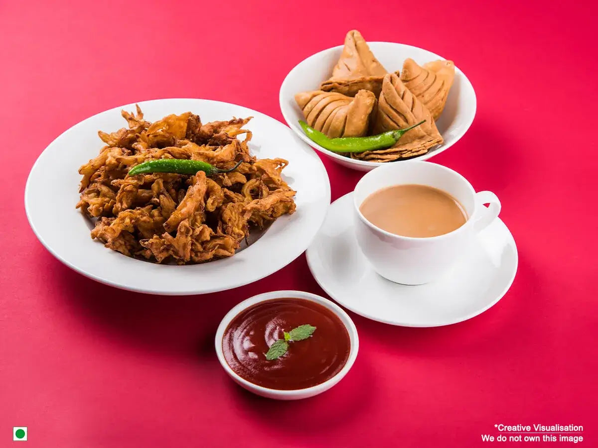 An image of samosas and bhajis kept on a plate beside a cup of tea. 