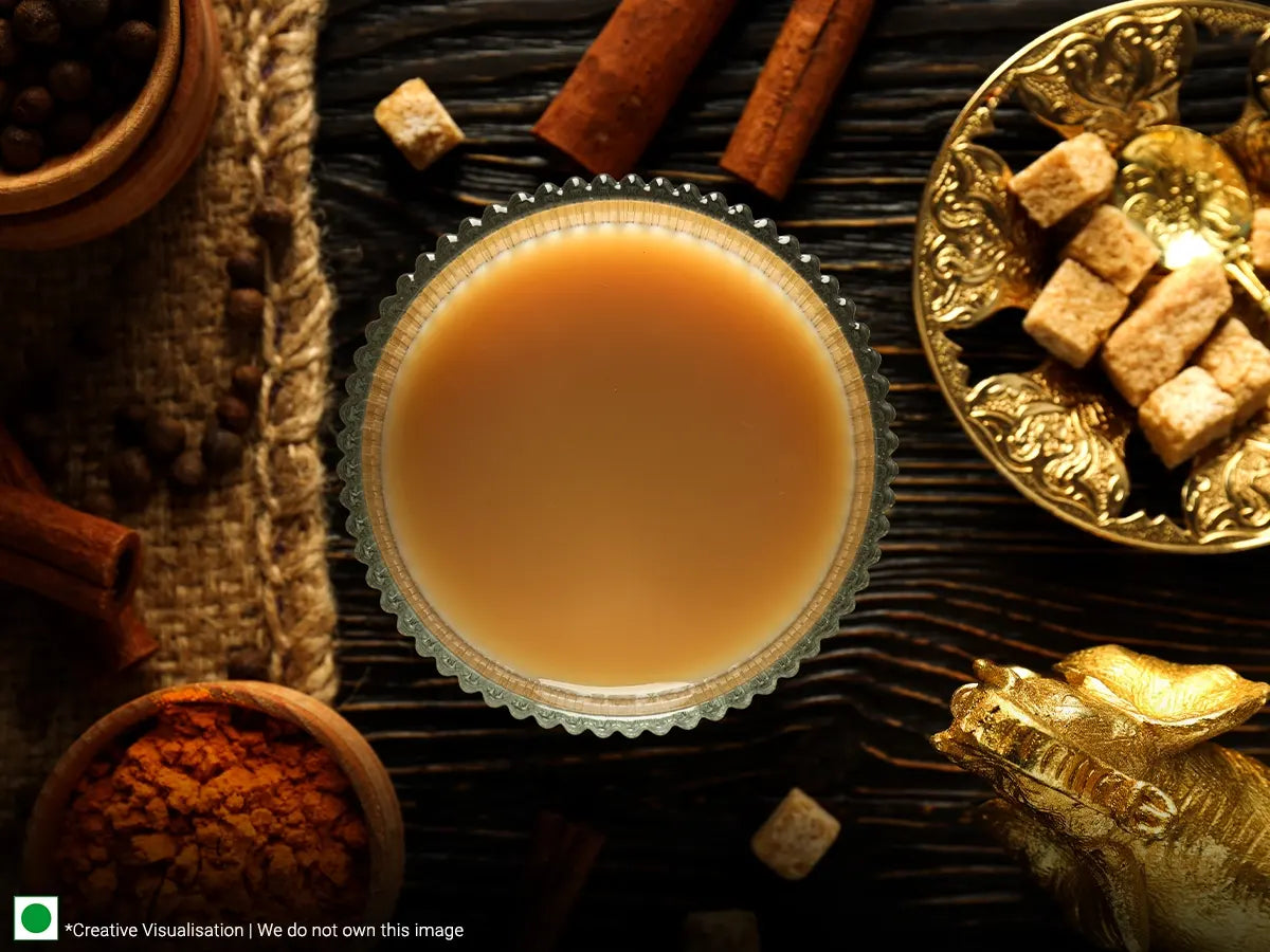 A cup of chai tea surrounded by various spices and sugar cubes.